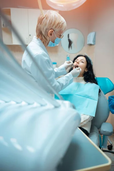 Bela morena encaracolado feminino dentista tratar paciente na clínica moderna — Fotografia de Stock