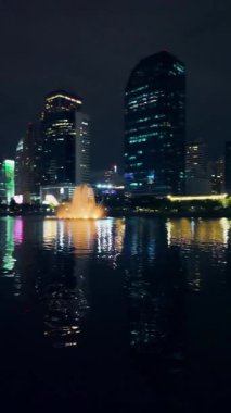 Bangkok gökdelenleri gece vakti Benchakitti Parkı 'ndan. Çeşme yansıması, şehir silüeti, akşam parıltısı Tayland şehri manzarası, modern mimari, 4k dikey video. Yüksek kaliteli görüntüler