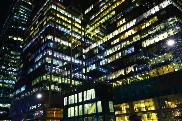Numerous offices where work continues at night, multi-colored window lights, white, dark building bulk with a multitude of windows.