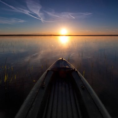 Kayık güneşe doğru yüzüyor. burun kayaklar bir şafak, sessiz bir göl, bir koyu mavi su yüzeyi ve mavi gökyüzü arka planı. Macera karşı hareket sembolü.