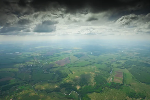 Dark clouds and green valley. Under the cloud, an aerial photograph from a great height, below the bottom edge of the clouds, below the green fields.