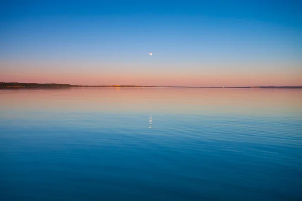 Turquoise sky dawn and turquoise water, the sun rises, Pleshcheyevo lake. smooth blue and turquoise lake surface at dawn, red and orange and sky blue.