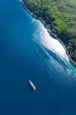Yeşil ormanlık uçurum (Cennet Adası) ve park etmiş bir yatı var.