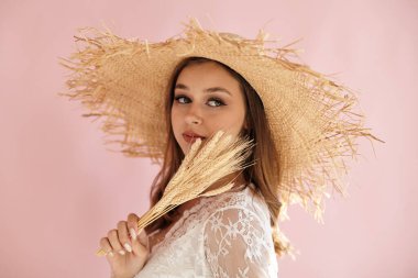 Pembe arka planda elinde buğdayla hasır şapkalı bir kız.