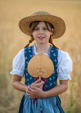 Geleneksel Bavyera Dirndl ve hasır şapka giyen sevimli liseli kız. Sıcak bir ışıkla portreyi kapat. Kültürel miras, çocukluk masumiyeti, halk kostümü, kırsal yaşam tarzı konsepti.