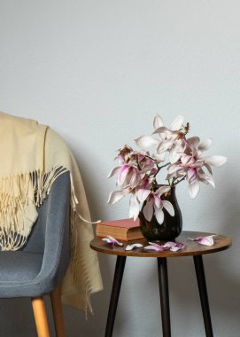 Modern sehpanın üzerinde, rahat kanepenin yanında vazoda duran zarif manolya çiçeği. Yumuşak ışıklandırma ve dekoratif çiçeklerle dekoratif ev dekorasyonu. Minimalist oturma odası detayı.