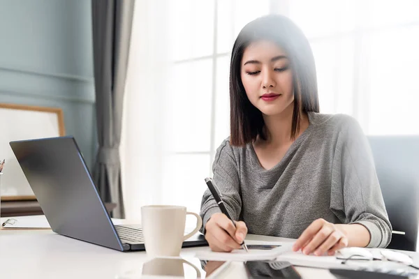 Asian working woman is writing a note on her office table. Working from home.