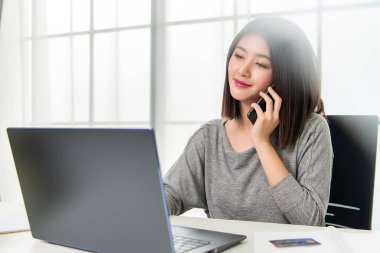 Asyalı çalışan kadın cep telefonuyla konuşuyor. Evde rahatça çalışıyorum. Ofiste çalışıyorum..