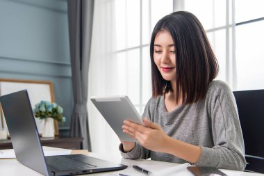 Asyalı çalışan kadın laboratuvarı ve tableti üzerinde çalışıyor. Evde rahatça çalışıyorum. Ofiste çalışıyorum..