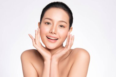 Güzel surat. Gülümseyen Asyalı kadın sağlıklı deri portresine dokunuyor. Güzel, mutlu bir kız modeli. Taze, nemli bir cildi ve beyaz arka planda doğal makyajı var.,