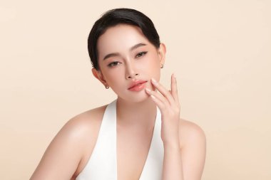 Güzel, genç bir Asyalı kadın, bej bir arka planda temiz, taze bir ten. Cilt bakımı, yüz bakımı, kozmetoloji, güzellik ve kaplıca. Asyalı bir kadının zarif bir portresi..