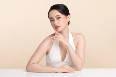 Güzel, genç bir Asyalı kadın, bej bir arka planda temiz, taze bir ten. Cilt bakımı, yüz bakımı, kozmetoloji, güzellik ve kaplıca. Asyalı bir kadının zarif bir portresi..