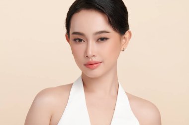 Güzel, genç bir Asyalı kadın, bej bir arka planda temiz, taze bir ten. Cilt bakımı, yüz bakımı, kozmetoloji, güzellik ve kaplıca. Asyalı bir kadının zarif bir portresi..