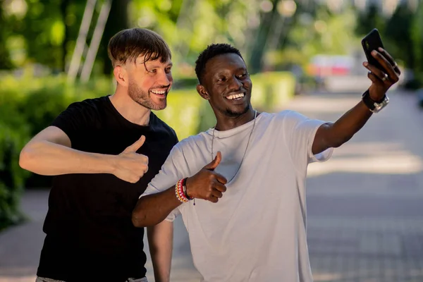 Black man and white man take a selfie on their smartphone and smile. Interracial friendship