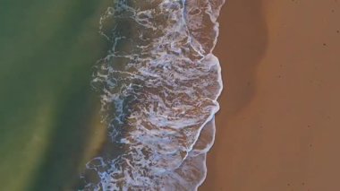 Sahile giren çıkan dalgaların olduğu tepeden aşağı statik bir video.