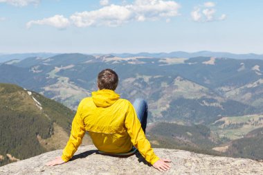Bir dağ manzarası arka planda büyük bir taş üzerinde oturan bir adam. Seyahat dağlarda kavramı