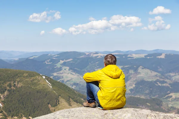 Bir dağ manzarası arka planda büyük bir taş üzerinde oturan bir adam. Seyahat dağlarda kavramı