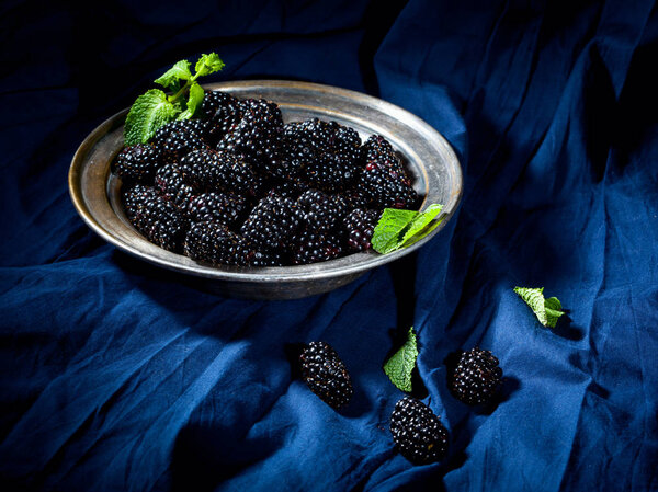 Vintage plate with blackberries and mint leaves on dark blue fabric