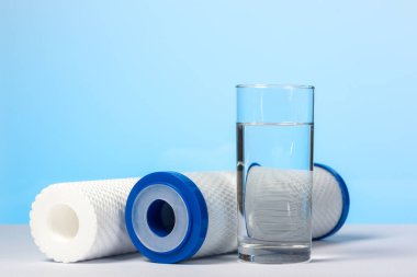 Bir bardak içme suyu ve evcil su arıtma sistemlerine açık mavi arka planda filtre kartuşları