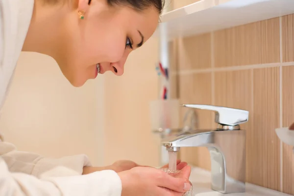 Young female washing her face in bathroom.