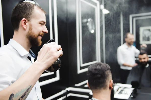 Young handsome barber making haircut of attractive man in barbershop.