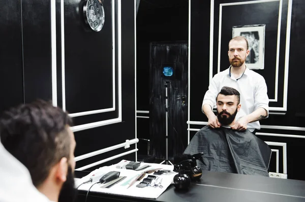 Master cuts hair and beard of men in the barbershop, hairdresser makes hairstyle for a young man.