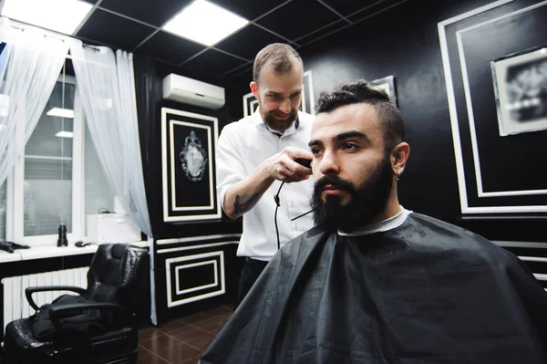 Master cuts hair and beard of men in the barbershop, hairdresser makes hairstyle for a young man.