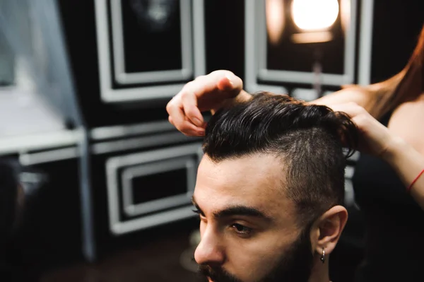 Master cuts hair and beard of men in the barbershop, hairdresser makes hairstyle for a young man.