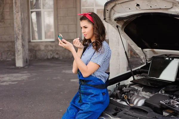 Cute attractive girl examining car engine at the auto repair shop.