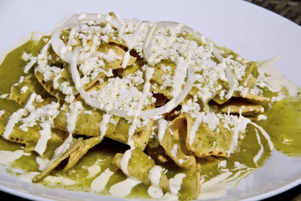 Green Chilaquiles with jalapeno green sauce, fresh crumbled cheese and sour cream, close-up.