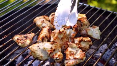 Salamura edilmiş tavuk filetosu dışarıda mangal kömüründe kızartılıyor. Şef et parçalarını diğer tarafa çevirmek için metal maşa kullanıyor. Yavaş çekim videosu 100fps. Yüksek kaliteli FullHD görüntüler