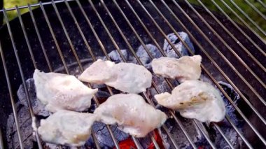Açık havada mangal kömüründe kızartılan çiğ soslu tavuk filetolarının yakın çekimi. Şef et parçalarını diğer tarafa atmak için metal maşa kullanıyor. Yavaş çekim videosu 100fps. Yüksek kaliteli FullHD görüntüler