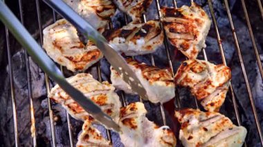 Terbiye edilmiş tavuk fileto parçaları dışarıda mangal kömüründe kızartılıyor. Şef et parçalarını diğer tarafa çevirmek için metal maşa kullanıyor. Yavaş çekim videosu 100fps. Yüksek kaliteli FullHD görüntüler