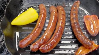Yakın plan. Yemek hazırlama. Biberli sosisler kızgın dökme demir bir tavada kızartılır. Aşçı sosisleri diğer tarafa metal maşayla çeviriyor. Yüksek kalite 4k görüntü