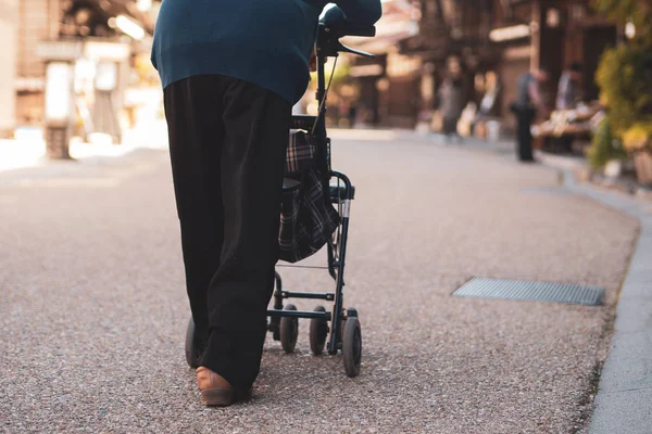 Japanese senior with a walking disability walking on street pushing her walker or wheel chair.