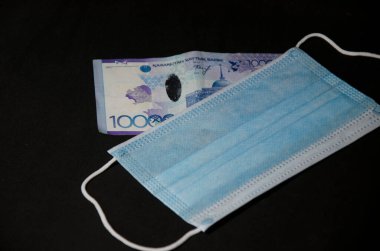 Notların kompozisyonu, Kazakistan madeni paraları ve siyah bir arka planda tıbbi maske. Kazak parası ve tıbbi maske..