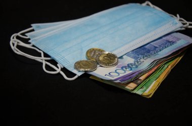 Notların kompozisyonu, Kazakistan madeni paraları ve siyah bir arka planda tıbbi maske. Kazak parası ve tıbbi maske..