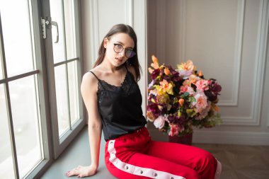 şık genç kadın kırmızı çiçekli kapalı pencere pervazına poz pantolon