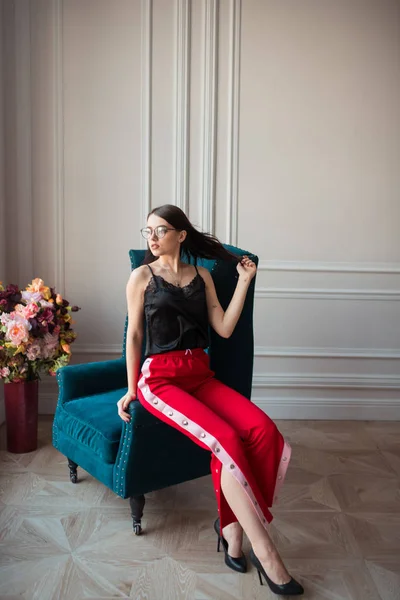 Stylish Young Woman Eyeglasses Red Pants Posing Armchair Indoors — Stock Photo, Image