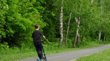 Ergen ormanda scooter 'a biniyor. Çocuk yolda sürmeyi öğreniyor..