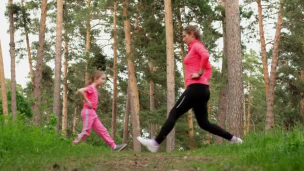 Jovem mãe esportiva e pequena filha fofa fazendo exercícios de fitness juntos em uma floresta . — Vídeo de Stock