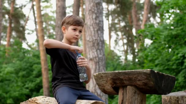 Мальчик пьет воду из бутылки после занятий спортом. Дети отдыхают после бега . — стоковое видео
