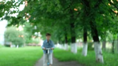 Küçük çocuk yazın mobilete biner. Çocuk parkta dinleniyor. Başparmaklar yukarı..