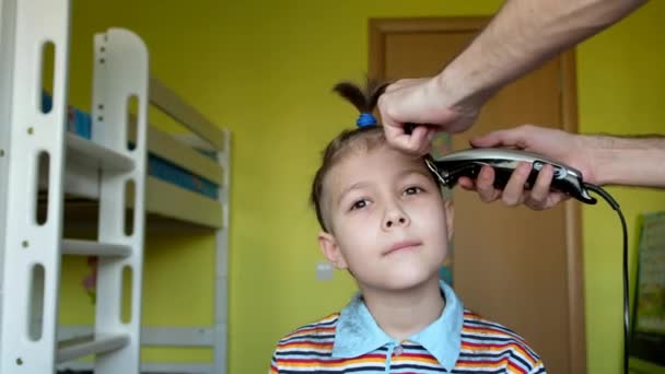 Vacker pojke i en frisersalong. Far klippte hår på lille son med klippare. Coronavirus, karantän, covid19. — Stockvideo