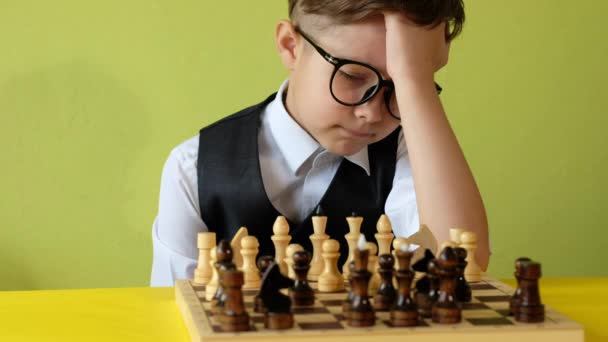 Çocuk masada satranç oynuyor. Gözlüklü küçük çocuk satranç stratejisi geliştiriyor, arkadaşıyla masa oyunu oynuyor.. — Stok video