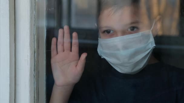 Kind in medizinischer Maske schaut aus dem Fenster und telefoniert. Selbstisolation in Quarantäne, Coronavirus, Covid19. — Stockvideo