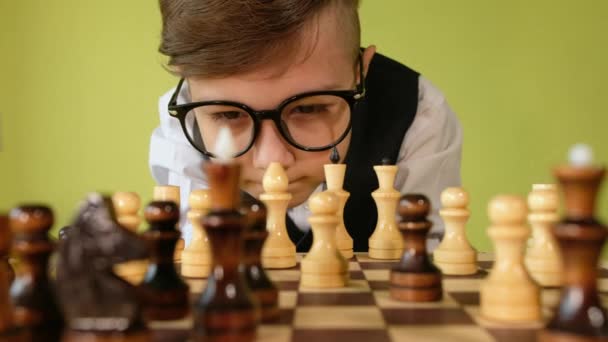 Criança a jogar xadrez à mesa. Menino com óculos desenvolvendo estratégia de xadrez, jogo de tabuleiro com amigo. — Vídeo de Stock