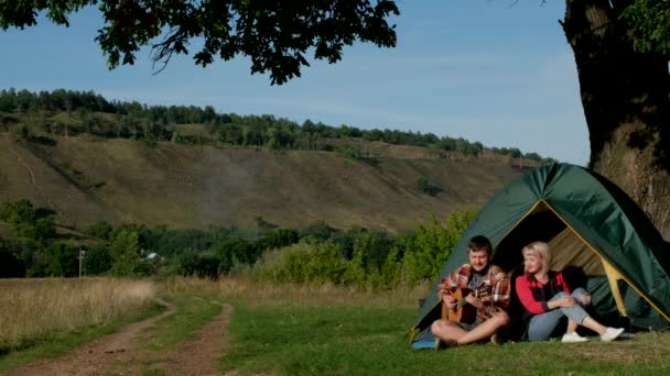 Mężczyzna i kobieta śpiewają piosenkę z gitarą siedzącą w namiocie. Rodzina jest na kempingu.. — Wideo stockowe