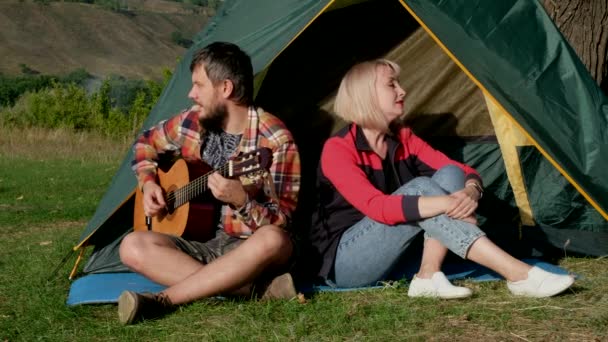Homme et femme chantent une chanson avec guitare assise à la tente. Famille est en voyage de camping. — Video