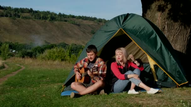 Uomo e donna cantano una canzone con la chitarra seduta alla tenda. La famiglia è in campeggio. — Video Stock